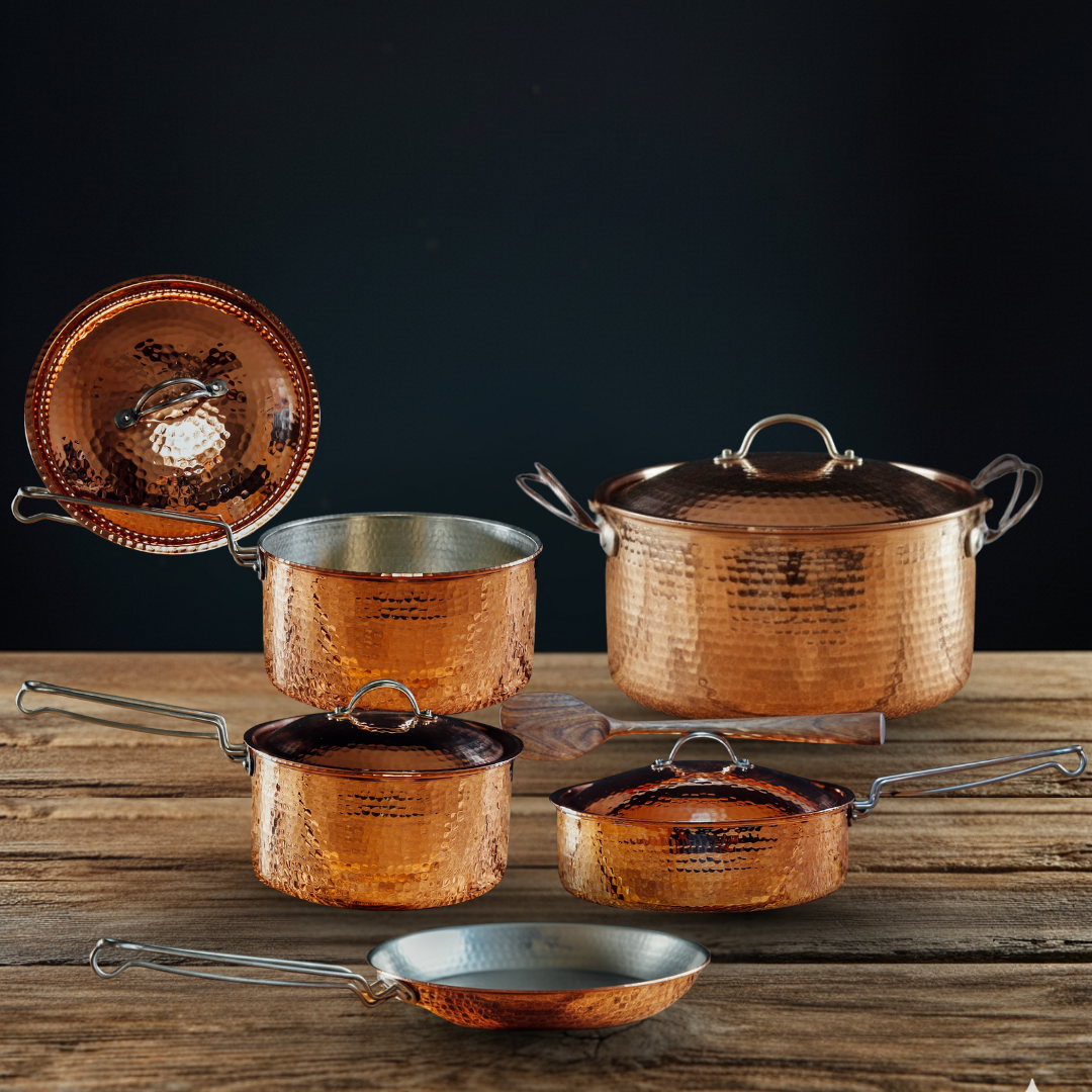 Set of copper cookware on a wooden surface with a dark background