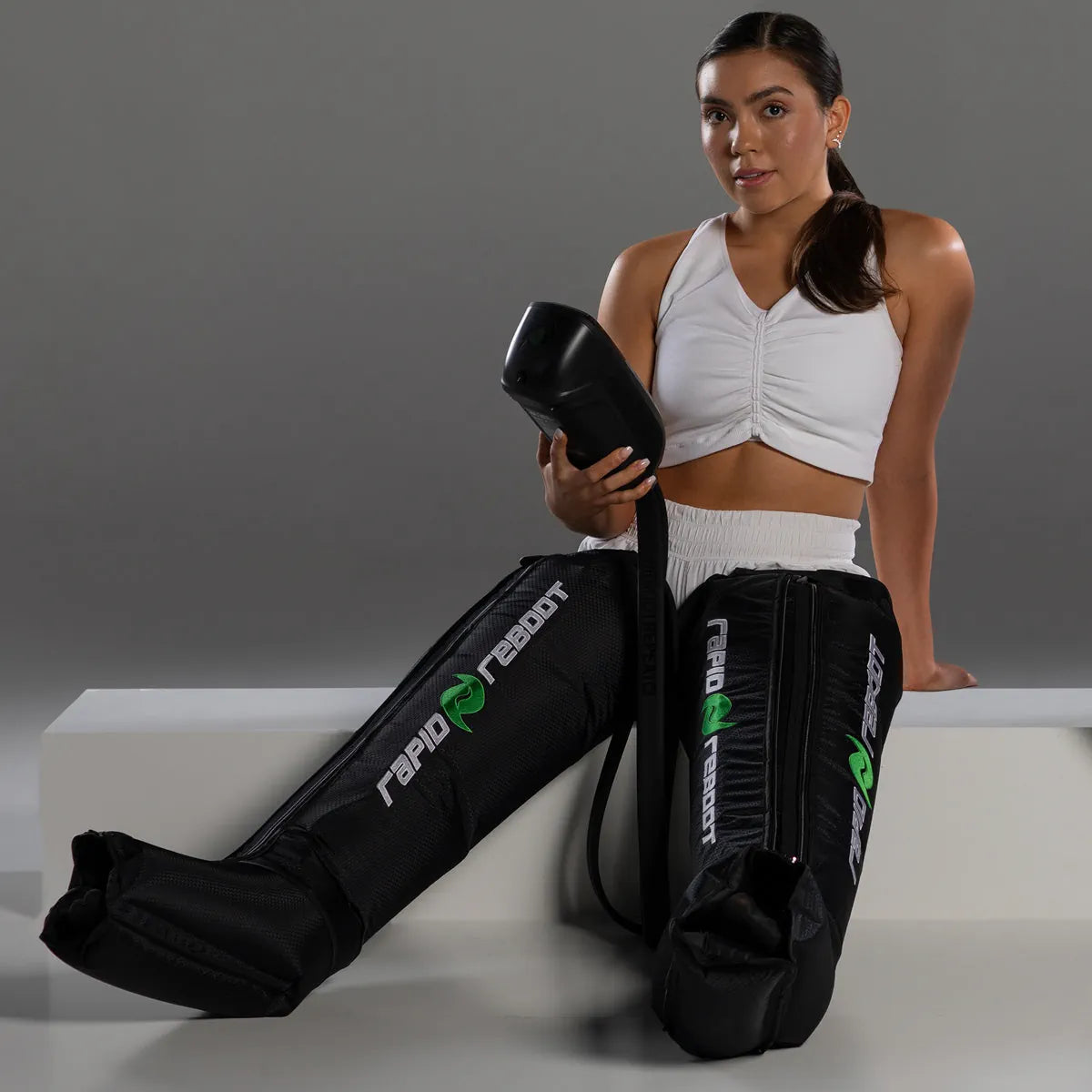 Woman wearing black compression boots with 'Rapid Reboot' branding on a gray background