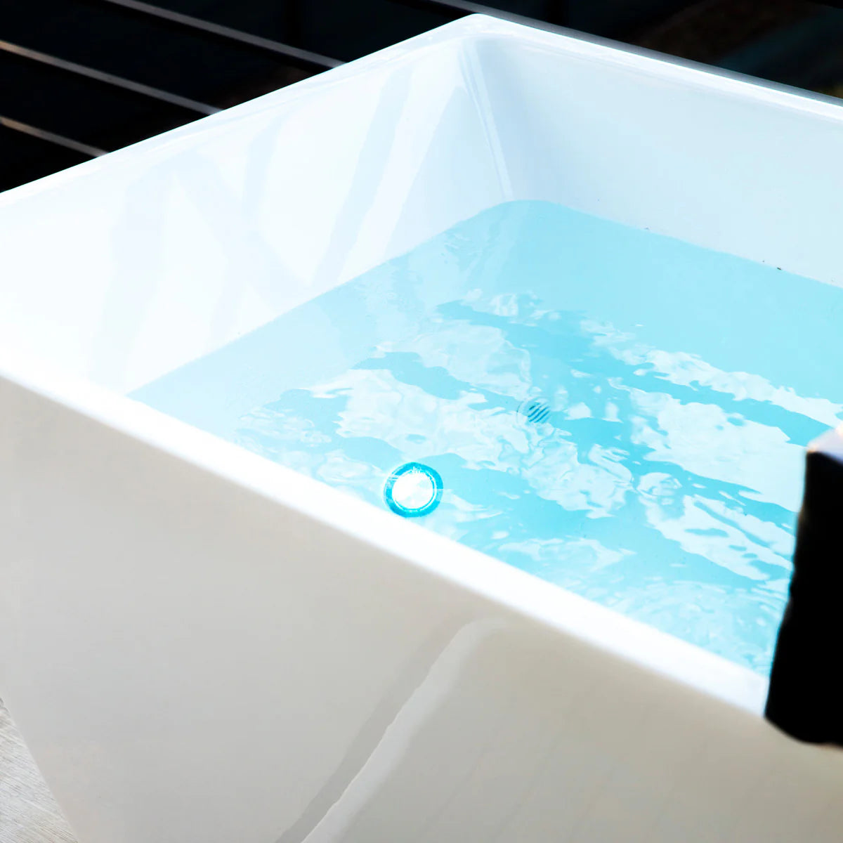 White bathtub with blue water and a black object partially submerged.