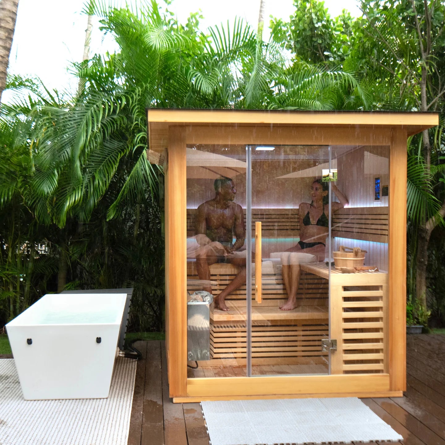 Two people in a wooden outdoor sauna surrounded by greenery