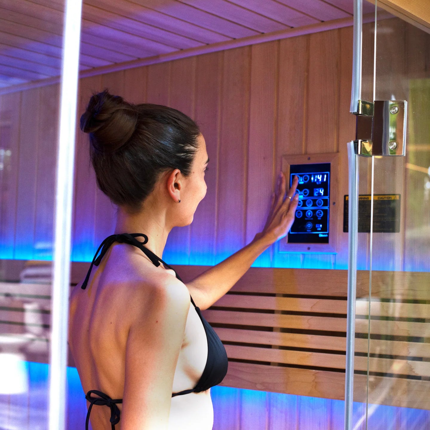 Woman in a black bikini interacting with a control panel in a infrared sauna.