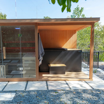 Modern outdoor sauna with wooden exterior and glass door, surrounded by greenery.