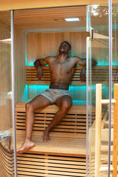 Man relaxing in a wooden sauna with glass walls.