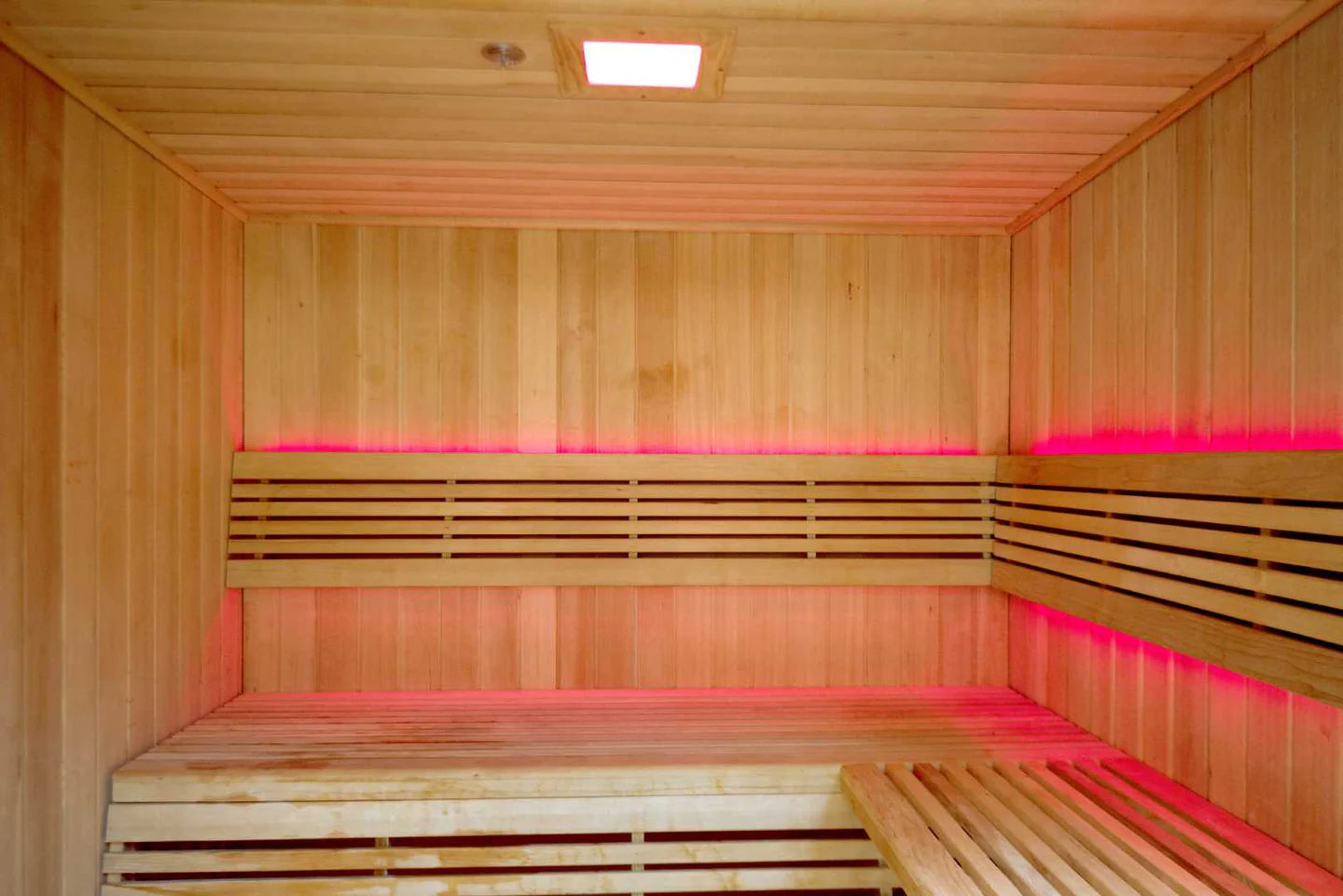 Wooden sauna with benches and pink LED lights on the walls.