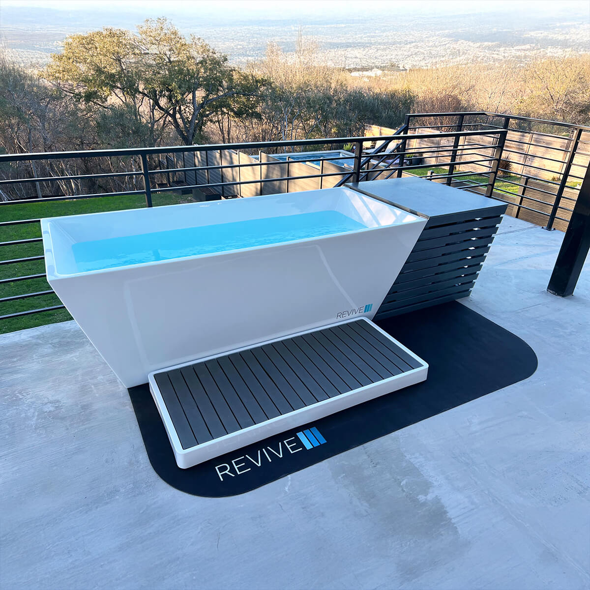 Outdoor cold tub with 'Revive' branding on a patio with scenic background