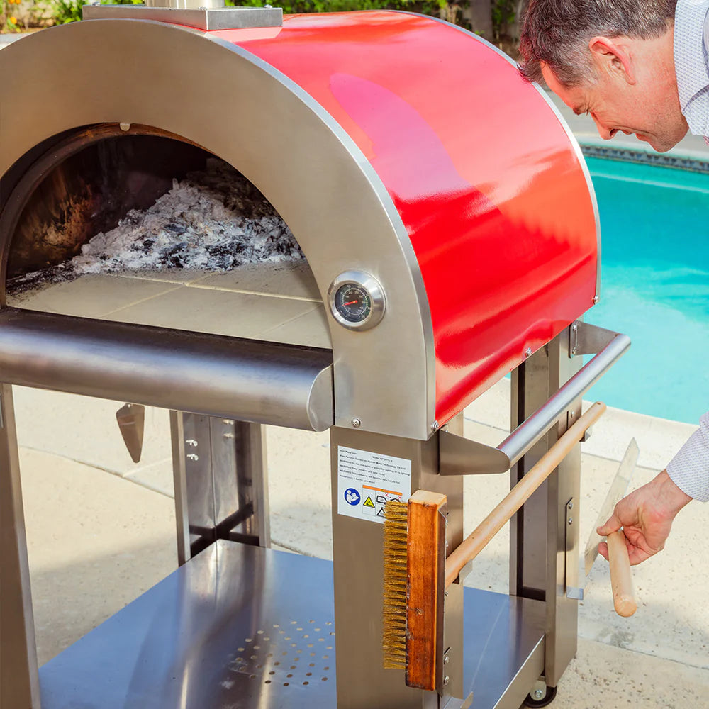 Person using a red and silver outdoor pizza oven by a pool.