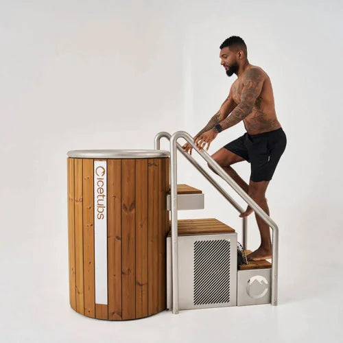 Man climbing into a wooden cold plunge on a light gray background