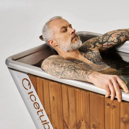 Man with tattoos relaxing in a wooden bathtub labeled 'Icetub'