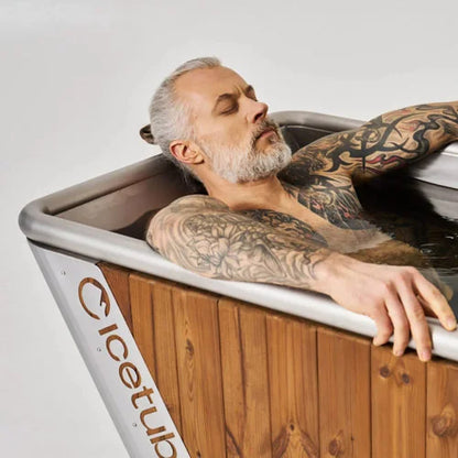 Man with tattoos relaxing in a wooden bathtub labeled 'Icetub'