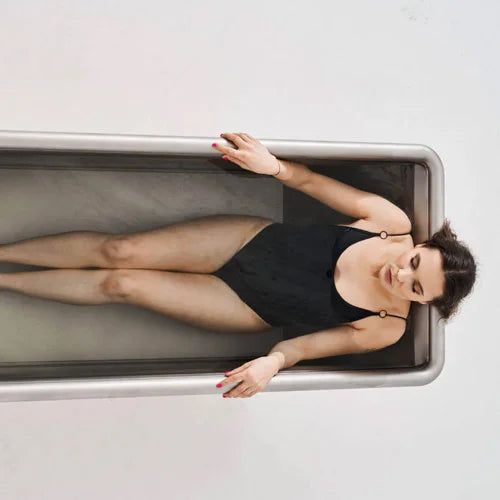 Woman lying in a stainless steel cold plunge with a neutral background