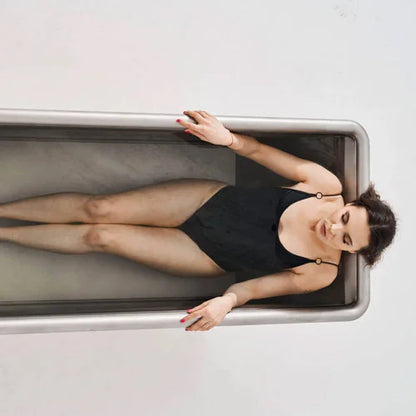 Woman lying in a stainless steel cold plunge with a neutral background