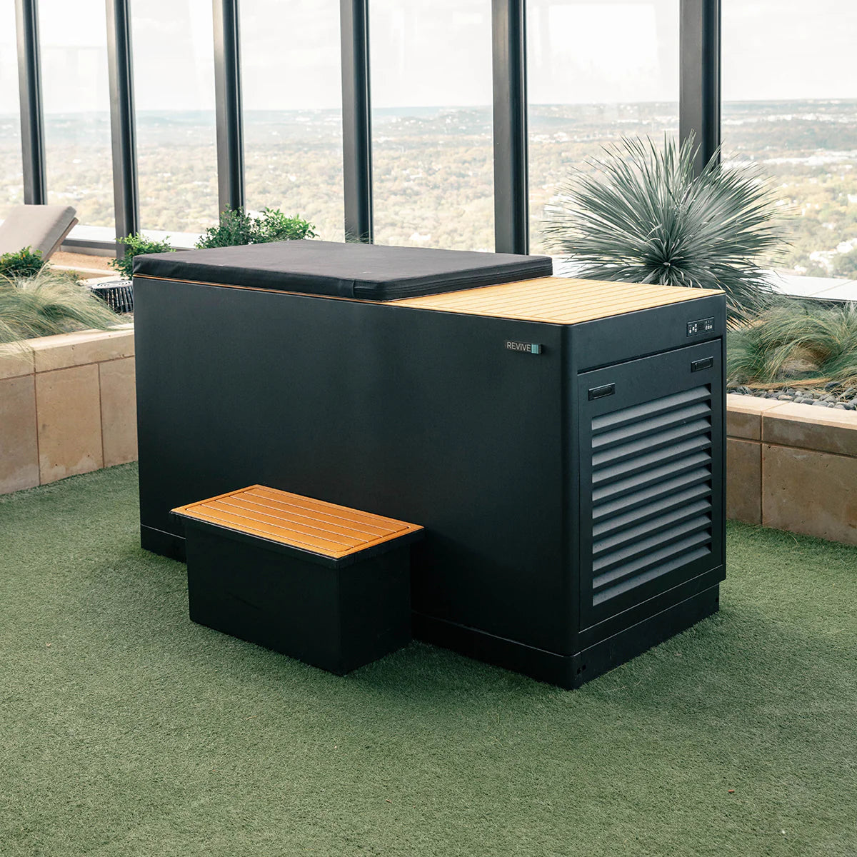 Black Cold tub  with wooden seats and table on a green lawn with a scenic view.