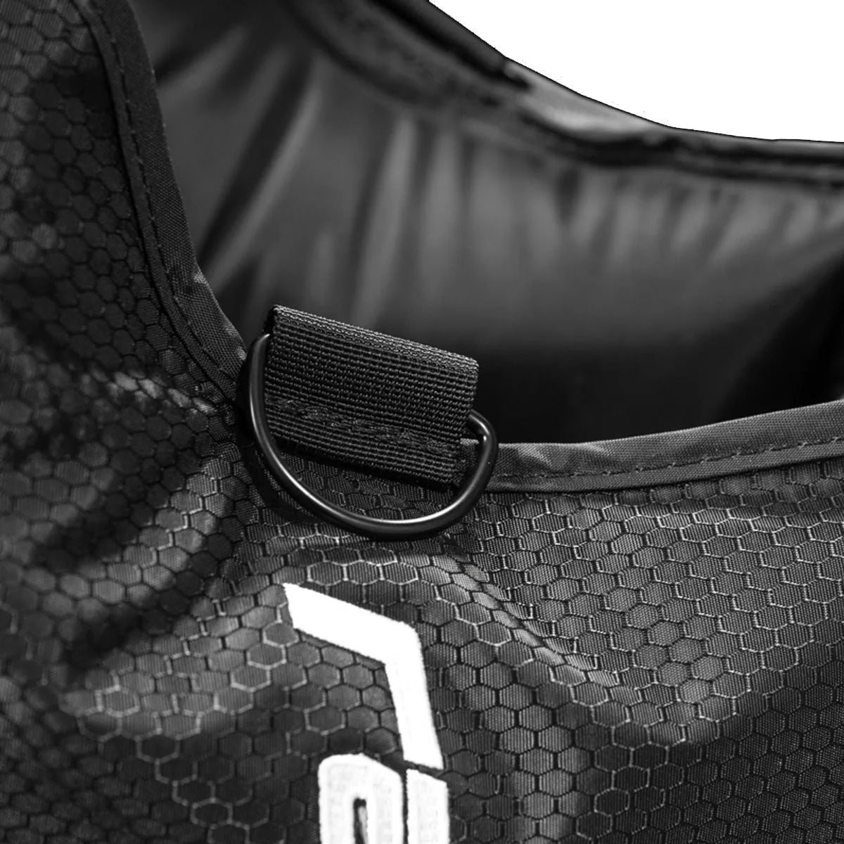Close-up of a black bag with a D-ring and hexagonal pattern, featuring a logo.