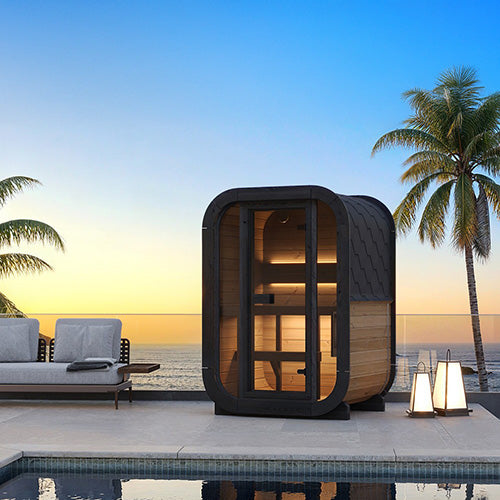 Outdoor sauna pod by a pool with palm trees and ocean view at sunset.