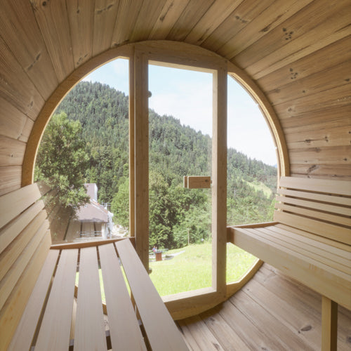 Wooden sauna with a large round window overlooking a green landscape