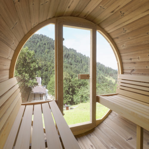 Wooden sauna with a large round window overlooking a forested area