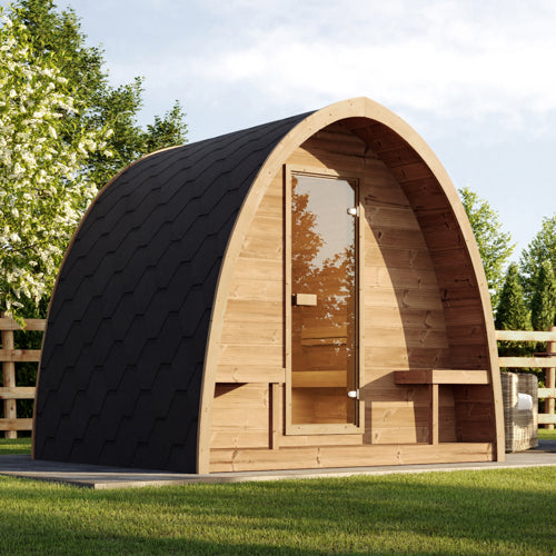 Wooden sauna with a black roof in a grassy area with trees in the background