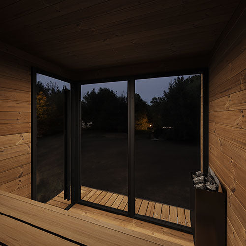 Wooden cabin interior with large glass windows overlooking a dark forest.