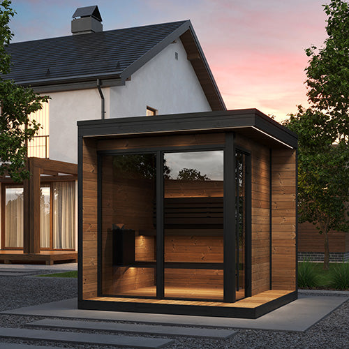 Modern wooden sauna with glass doors in front of a house during sunset.