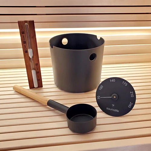 Black sauna bucket and ladle with a thermometer on a wooden surface