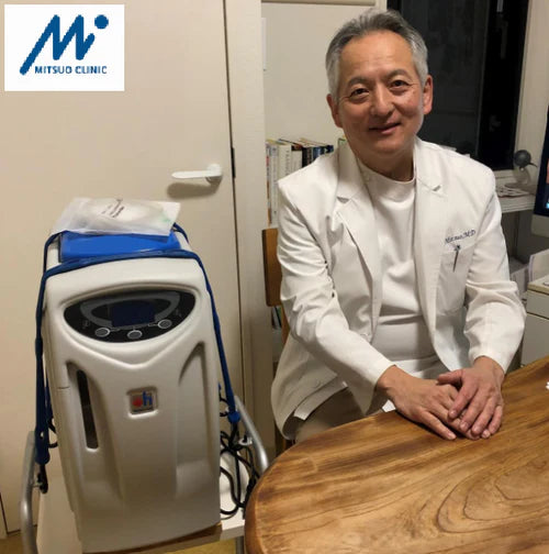 Person in a white coat sitting next to an hydrogen inhalator with Mitsuwo Clinic logo.