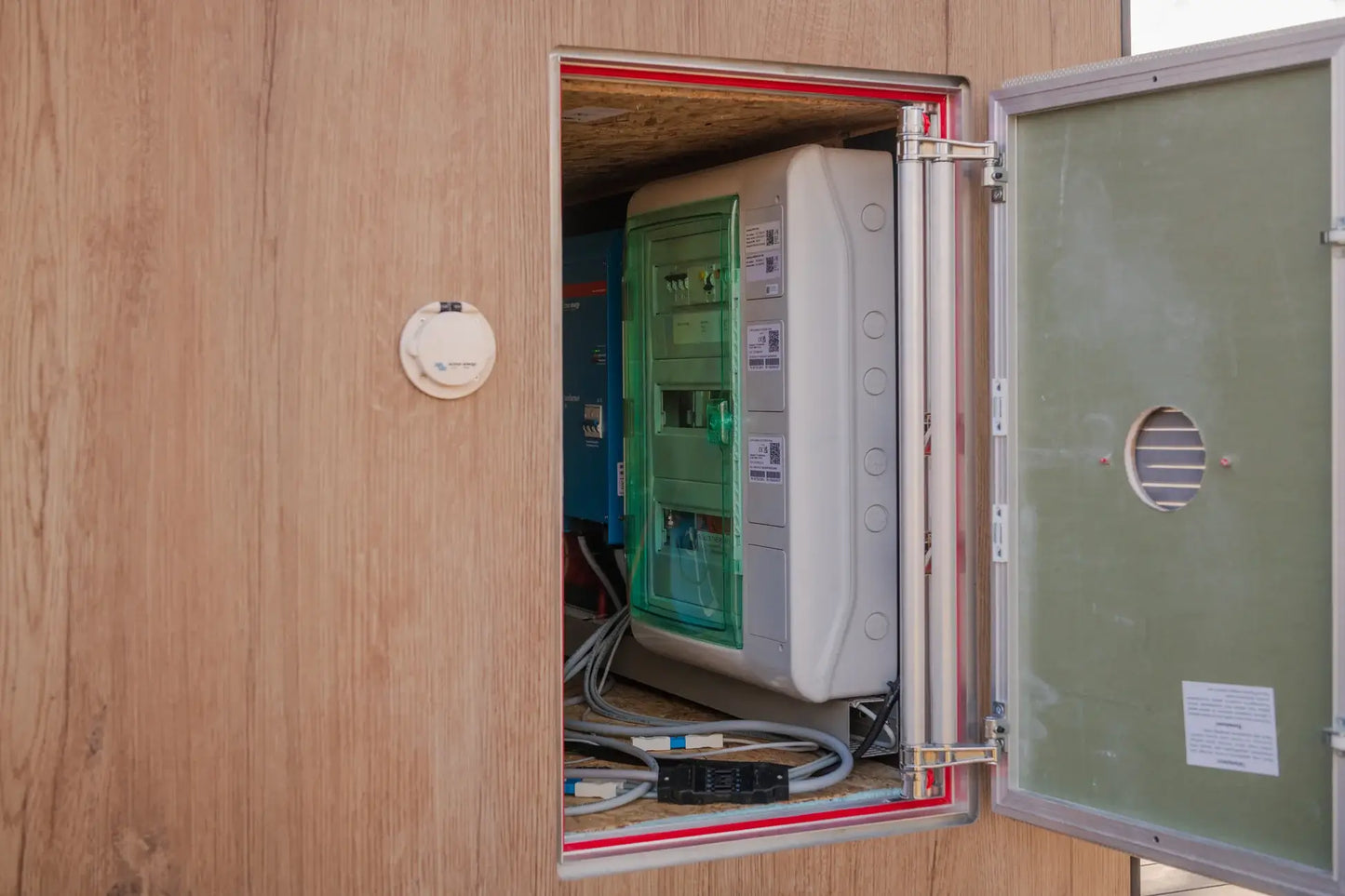 Open electrical panel with various components inside a wooden wall.
