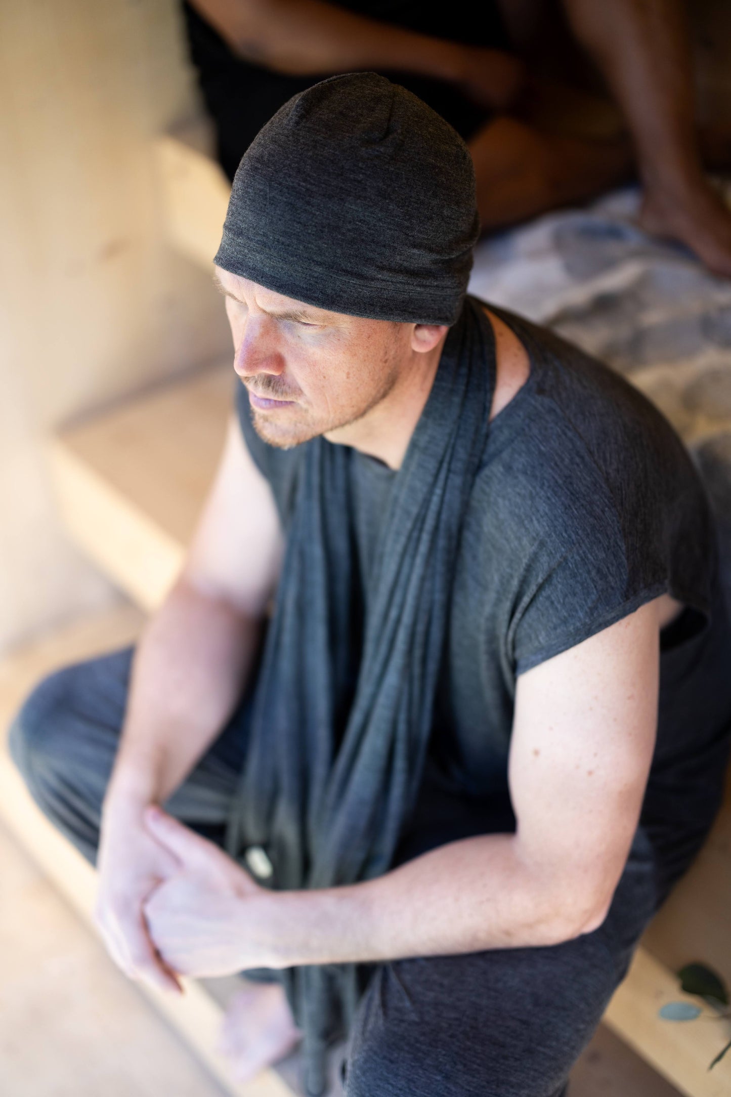 Man sitting on a wooden floor wearing a grey beanie and grey clothing.