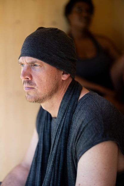 Man wearing a black merino wool beanie and grey clothing sitting against a neutral background