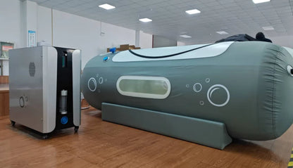 Large inflatable hyperbaric chamber and smaller machine on a wooden floor in a room with tiled ceiling.
