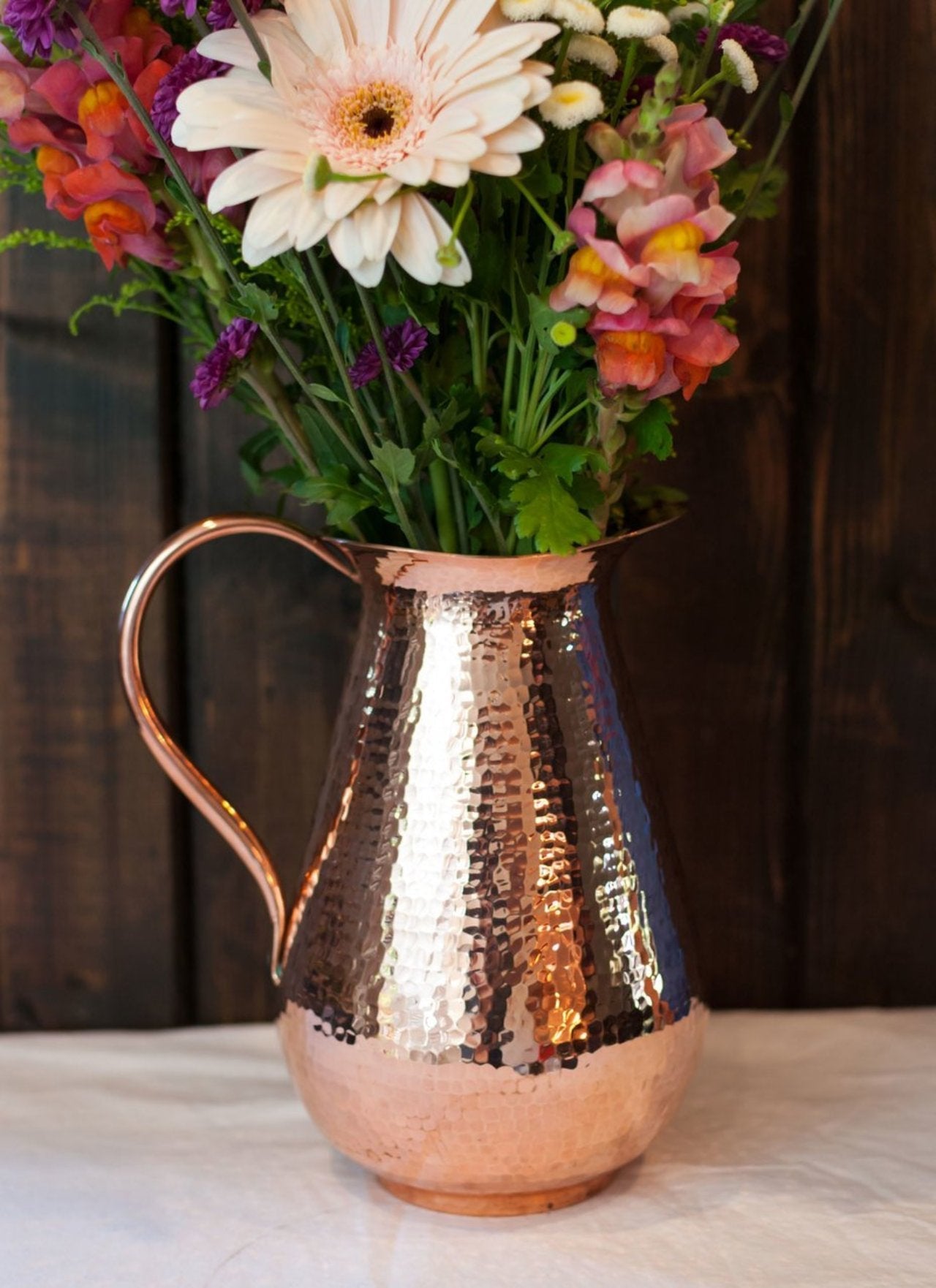 Copper pitcher with flowers against a wooden background