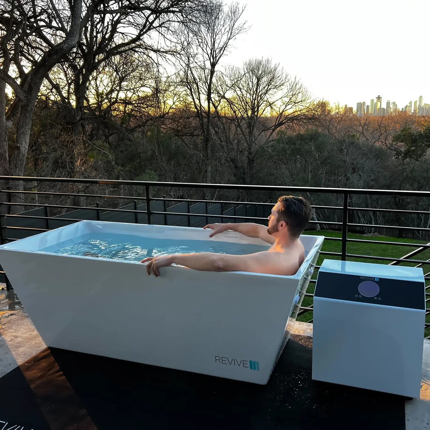 Man relaxing in an outdoor bathtub labeled 'REVIVE' with a scenic background