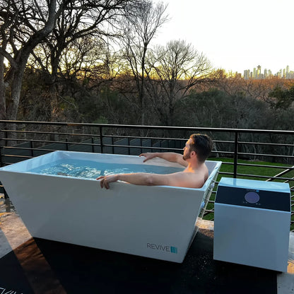 Man relaxing in an outdoor bathtub labeled 'REVIVE' with a scenic background