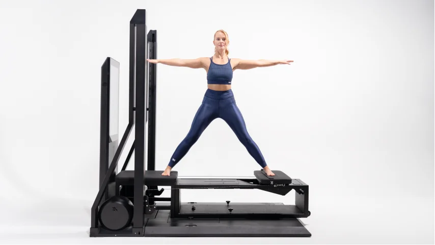 Woman exercising on a Pilates reformer machine against a white background