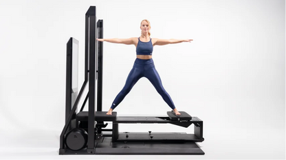 Woman exercising on a Pilates reformer machine against a white background