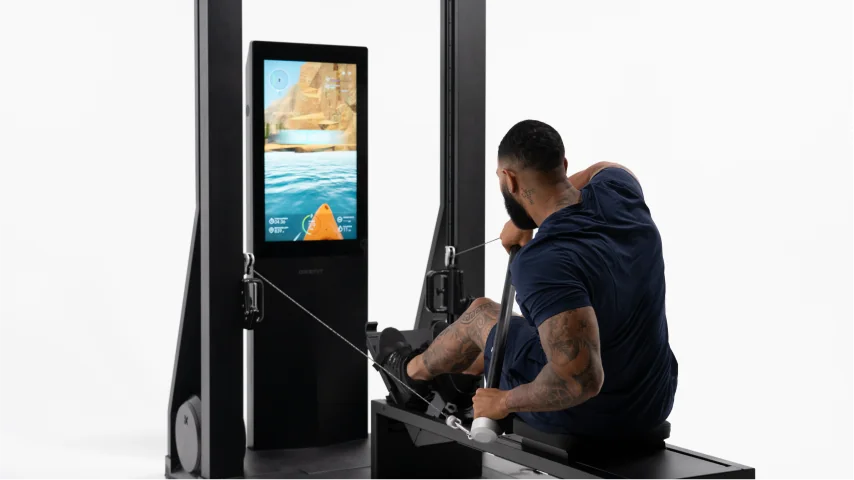 Person using a Pilates reformer machine with a screen displaying an ocean scene.