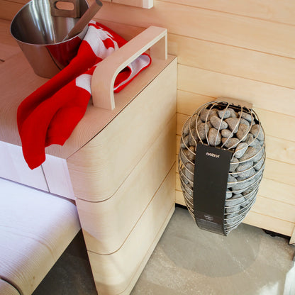 Sauna interior with wooden bench, red towel, metal bucket, and Harvia heater.