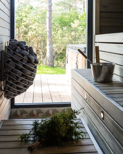 Wooden sauna interior with stones, bucket, and greenery.