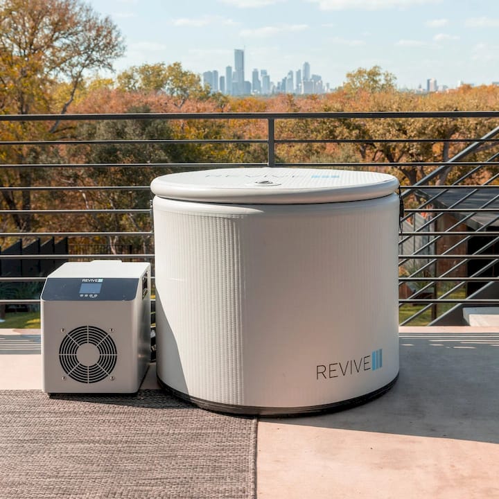 Cold tub with 'REVIVE' branding on a rooftop with a city skyline in the background.