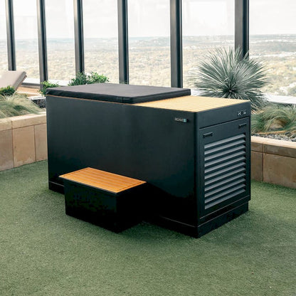 Black Cold tub  with wooden stairs on a green lawn with a scenic view.