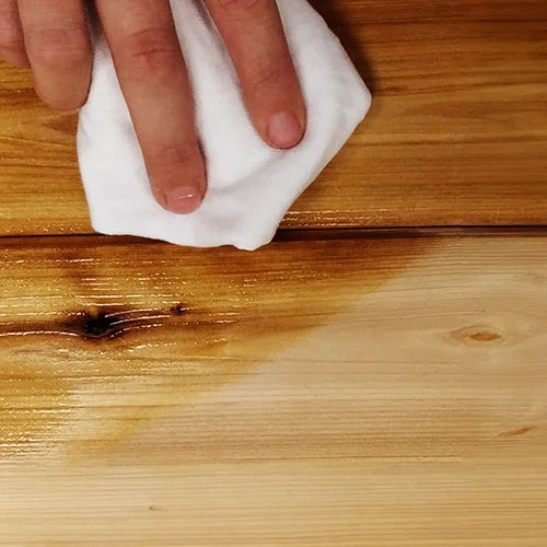 Hand using a white cloth to wipe a wooden surface
