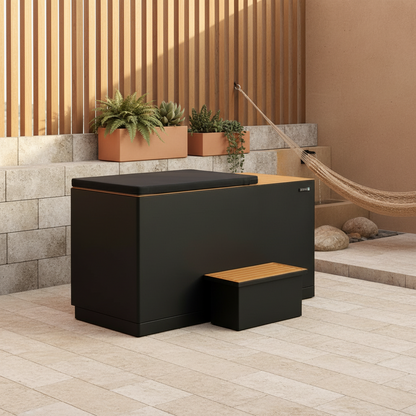 Black outdoor cold tub with wooden step on a patio with plants and a hammock.